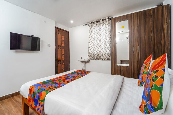 Quarto de hotel com cama, televisão na parede, pia e guarda-roupa de madeira.