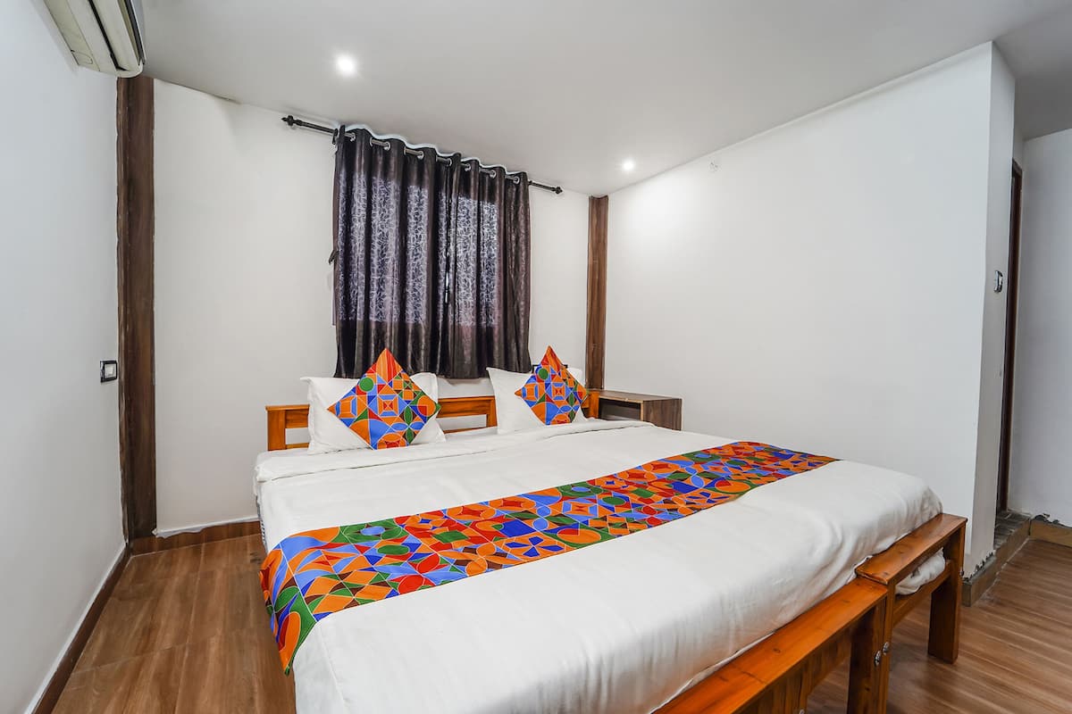 A neatly made bed with a colorful bedspread, a wooden bench, and a window with curtains.