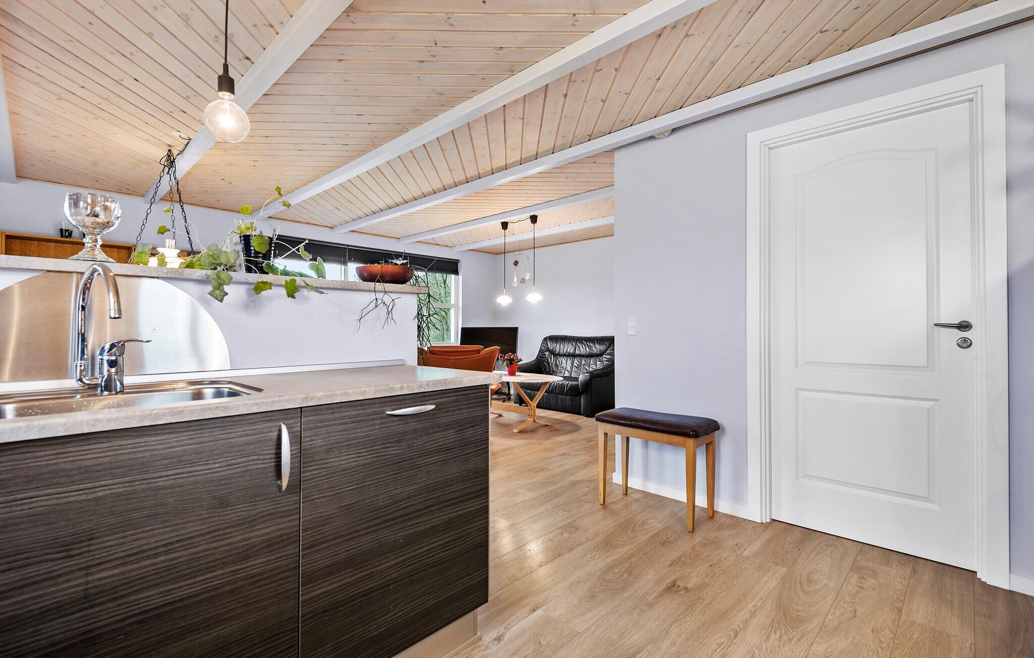 A modern kitchen with wooden ceiling beams, a stainless steel sink, and a black leather chair.