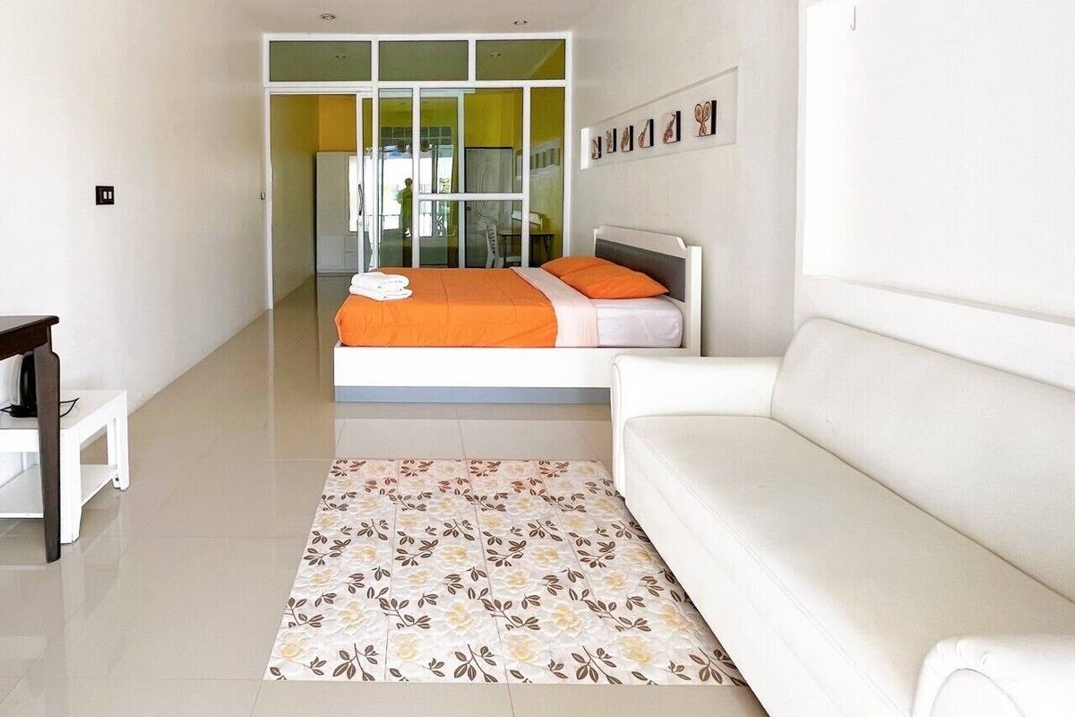 A modern hotel room with a large bed, white walls, a white sofa, and a patterned rug.