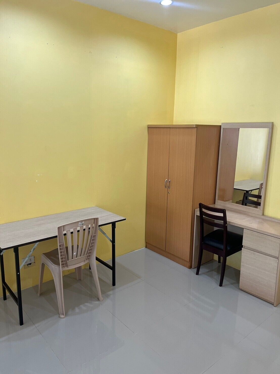 A room with a desk, two chairs, a wardrobe, and a mirror.