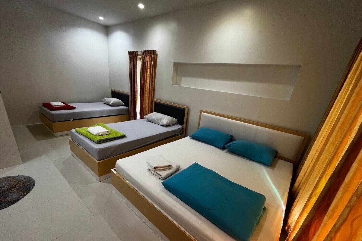 A modern hotel room with two single beds and a larger bed. The room has a minimalist design with neutral colors and a clean layout.
