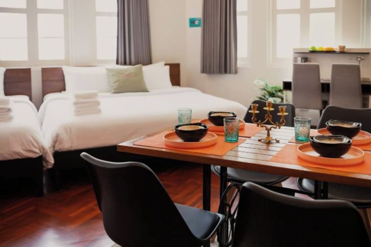 A hotel room with two beds, a dining table with bowls and glasses, and a view of the outside through large windows.