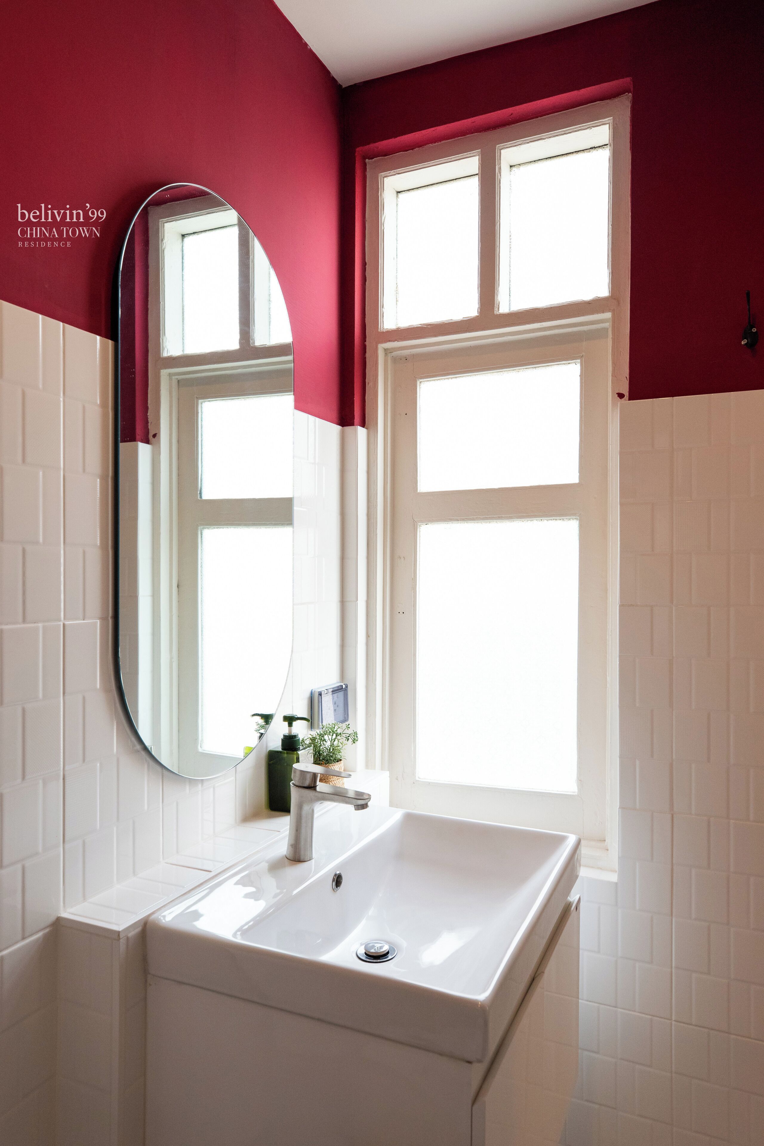A bathroom with a white sink, a mirror, and a window with red curtains.