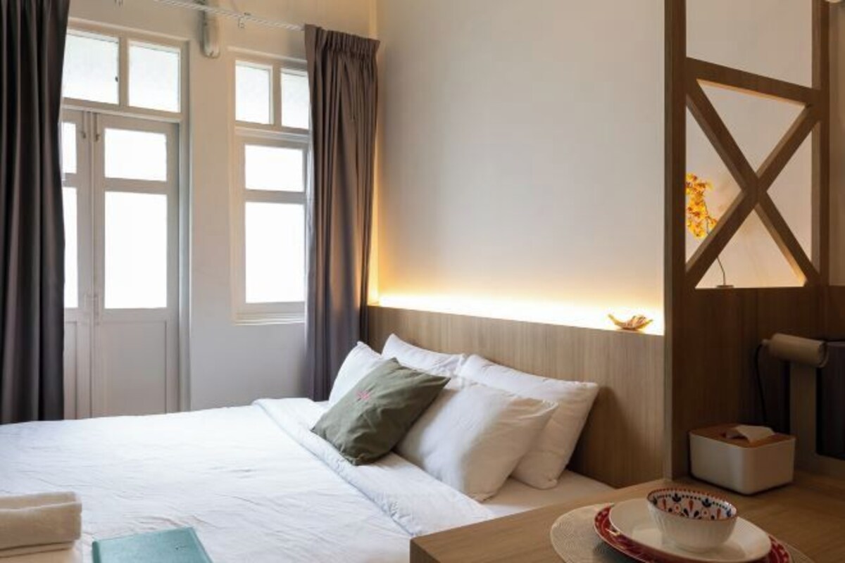 A hotel room with a bed, a bedside table with a bowl, and a window with curtains.