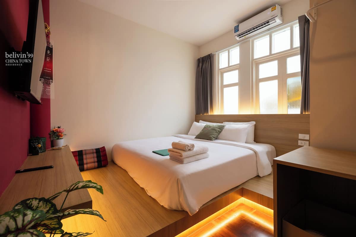 Een hotelkamer met een bed, nachtkastje en een raam met gordijnen.