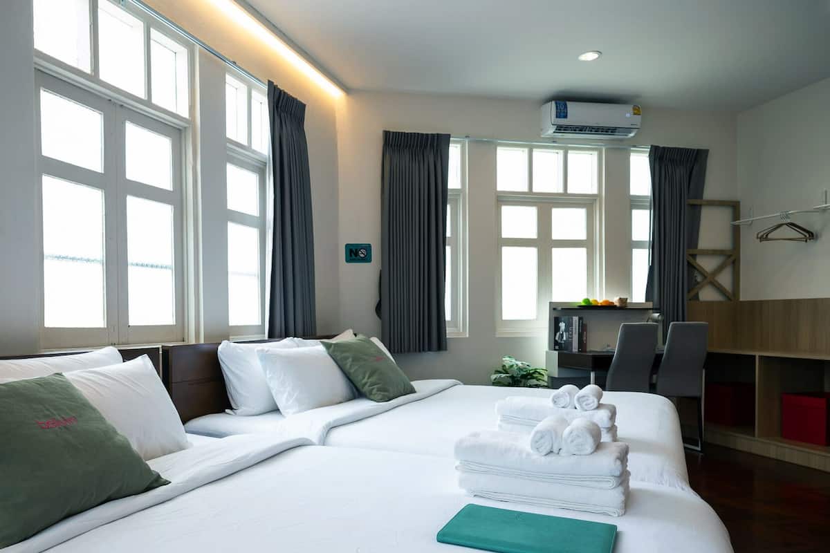 Een hotelkamer met een groot bed, twee ramen met gordijnen, een bureau met stoel en een wandairconditioner.