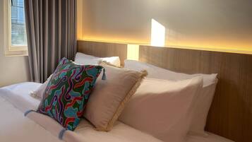 A hotel room with a neatly made bed, a window with curtains, and a wall-mounted light fixture.