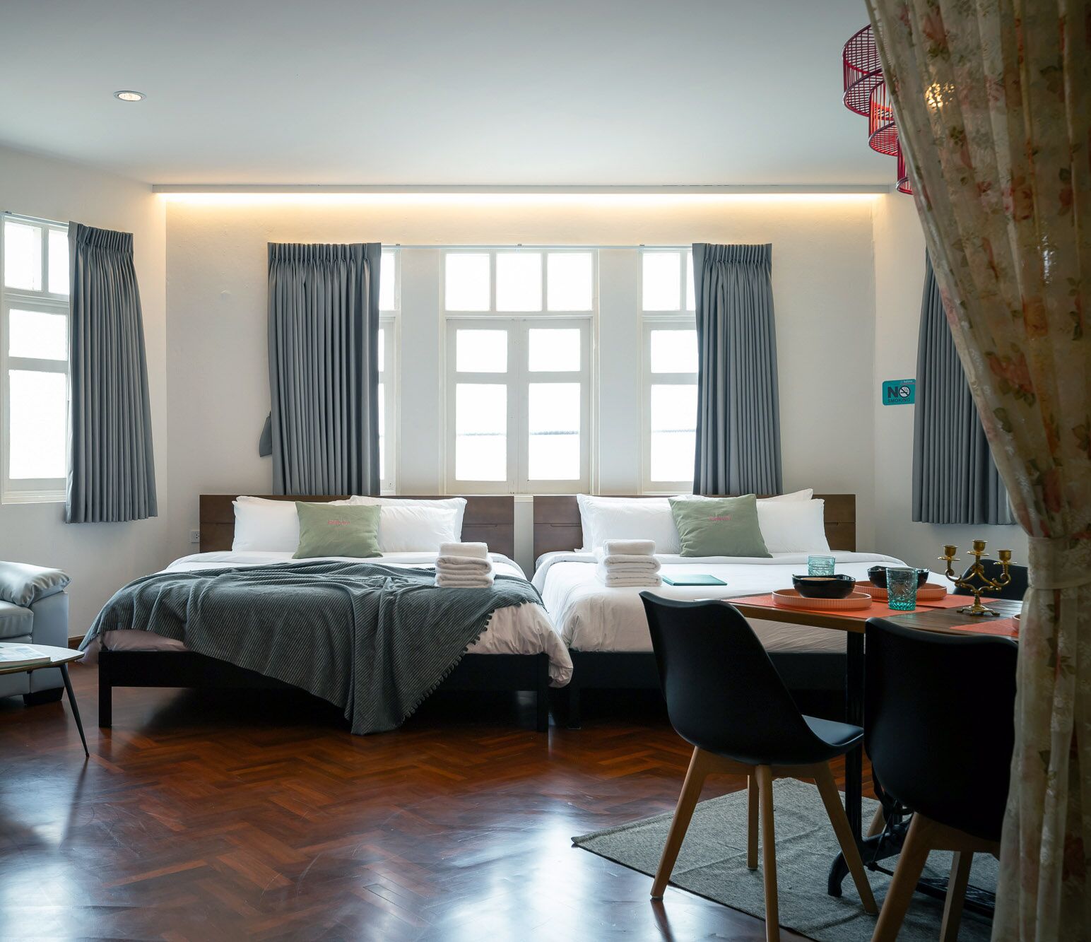 A hotel room with two beds, a desk with chairs, and a view of the sea through large windows.