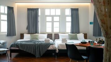 A hotel room with two beds, a desk with chairs, and a view of the sea through large windows.