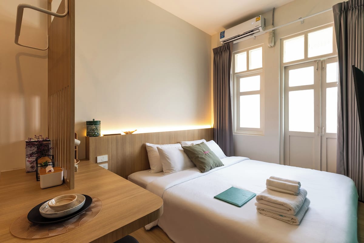 Een hotelkamer met een bed, nachtkastje en een raam met gordijnen.