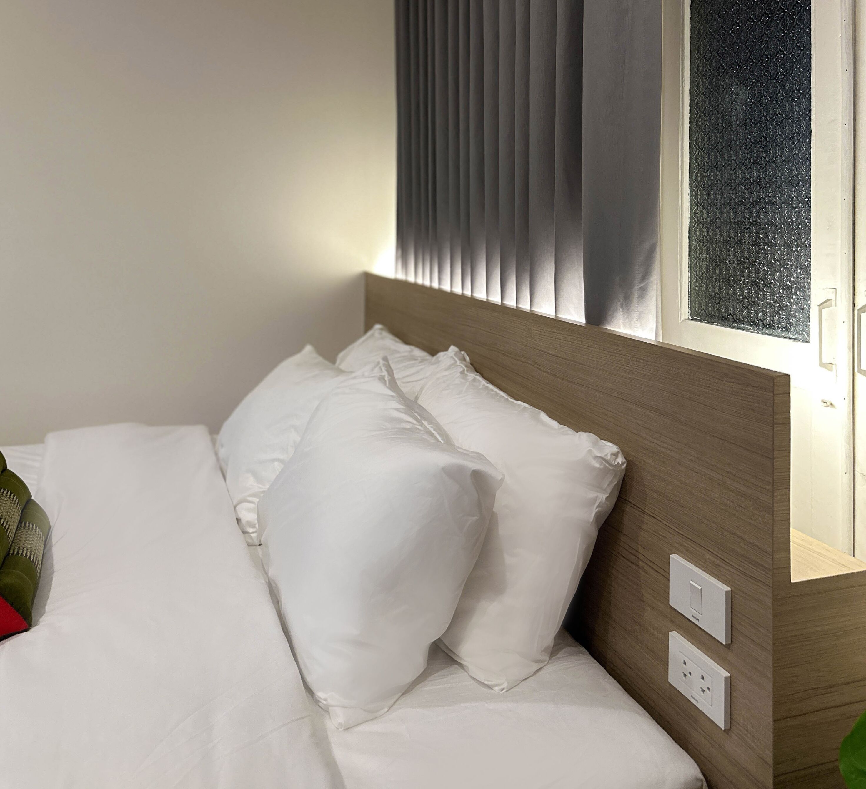 Ein ordentlich bezogenes Bett mit weißen Leinen und Kissen, ein hölzernes Kopfteil und ein Fenster mit Jalousien.