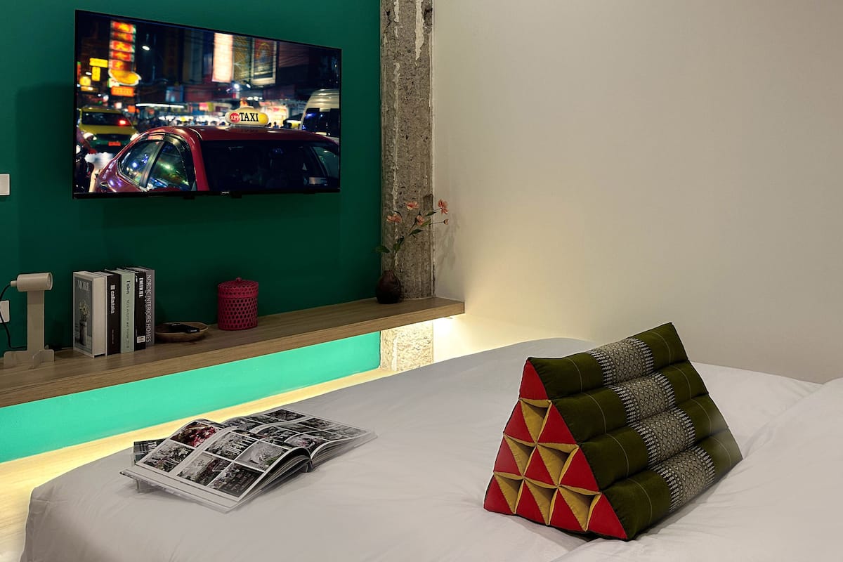 Hotelkamer met een bed, een televisietoestel waarop een stadsbeeld te zien is, een tijdschrift en een plank met boeken en een rode mand.