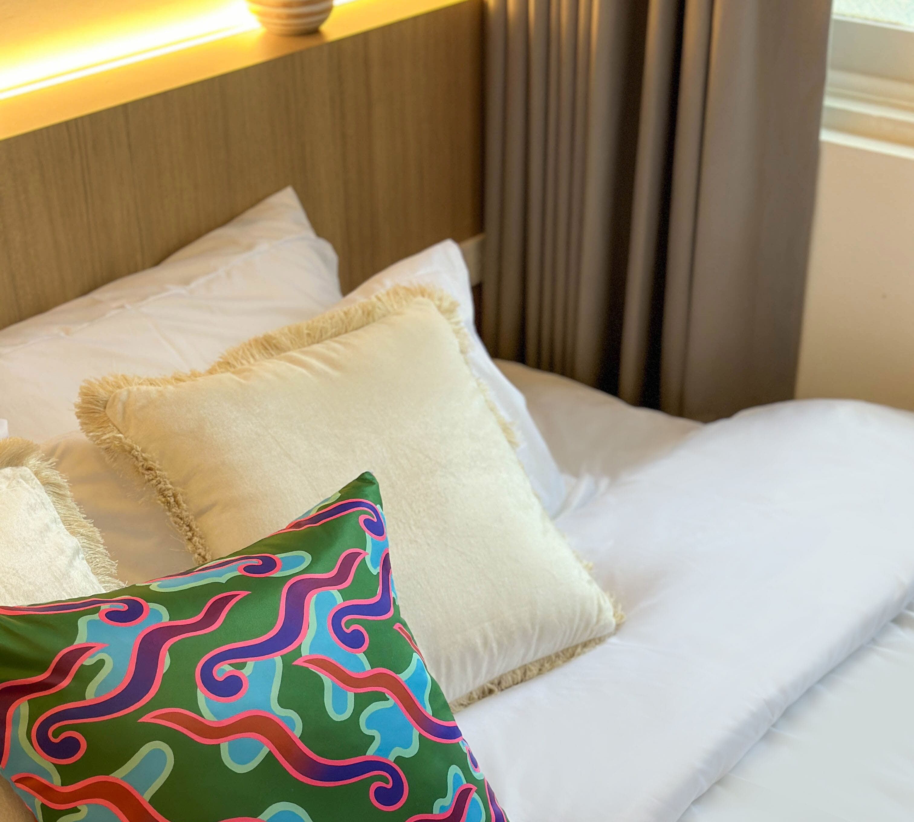 A neatly made bed with white linens and multiple pillows, including a colorful one.