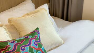 A neatly made bed with white linens and multiple pillows, including a colorful one.