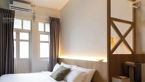 A hotel room with a bed, a bedside table with a lamp, a window, and an air conditioning unit.