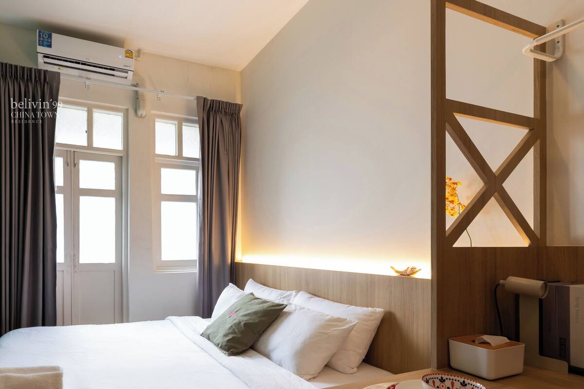 Een hotelkamer met een bed, een nachtkastje met een lamp, een raam en een airconditioner.