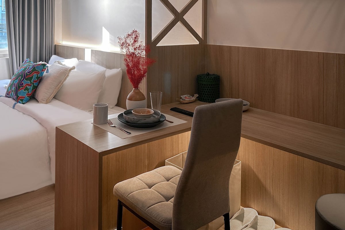Hotelkamer met een bed, een bureau met stoel, een vaas met rode bloemen, een schaal en een kledingrek.