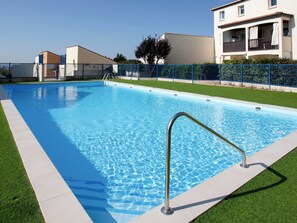 Une piscine rectangulaire à l’eau d’un bleu limpide, entourée d’une clôture métallique et d’une zone herbeuse.