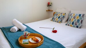 A neatly made bed with a teal blanket, a tray with a pastry, a rose, and a small table with a cup and a postcard. - Port Saint-Jacques by Interhome (La Bernerie-en Retz)