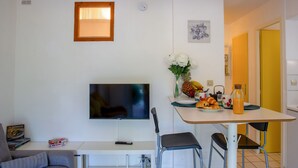 A modern living room with a flat-screen TV, a sofa, a dining table with chairs, and a kitchen area with a yellow door. - Port Saint-Jacques by Interhome (La Bernerie-en Retz)