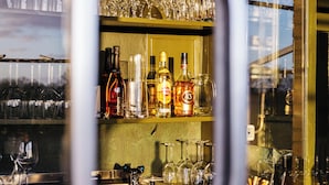 A bar area with shelves of wine bottles and glasses, a coffee cup, and a view through a window. - Zollhoes; Find the border! On discovery in the border area NL/DE (Haren (Ems))