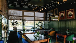 A restaurant interior with wooden tables and chairs, potted plants, and framed pictures on the walls. - Zollhoes; Find the border! On discovery in the border area NL/DE (Haren (Ems))