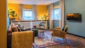 A living room with a sofa, armchairs, a coffee table, and a TV mounted on the wall. - Zollhoes; Find the border! On discovery in the border area NL/DE (Haren (Ems))