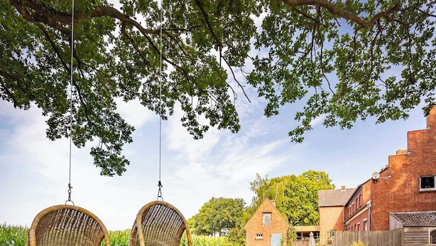 Two wicker chairs hanging from a tree, a brick building, and a grassy yard. - Zollhoes; Find the border! On discovery in the border area NL/DE (Haren (Ems))