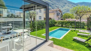 A modern villa with a glass-enclosed patio, a swimming pool, and a mountain backdrop.