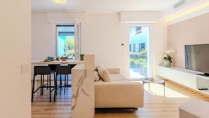 A modern living room with a sofa, a TV, and a dining area with chairs and a table.