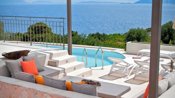 A poolside area with a view of the sea, a white outdoor sofa with cushions, and a small table. - Casa di CLO sea front stone property,private pool, Fiscardo 500 m (Borgo Fiskardo)