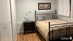 A bedroom with a bed, a nightstand, a lamp, and a framed picture on the wall. - Cozy One Bed Suite Near Beach (White Rock)