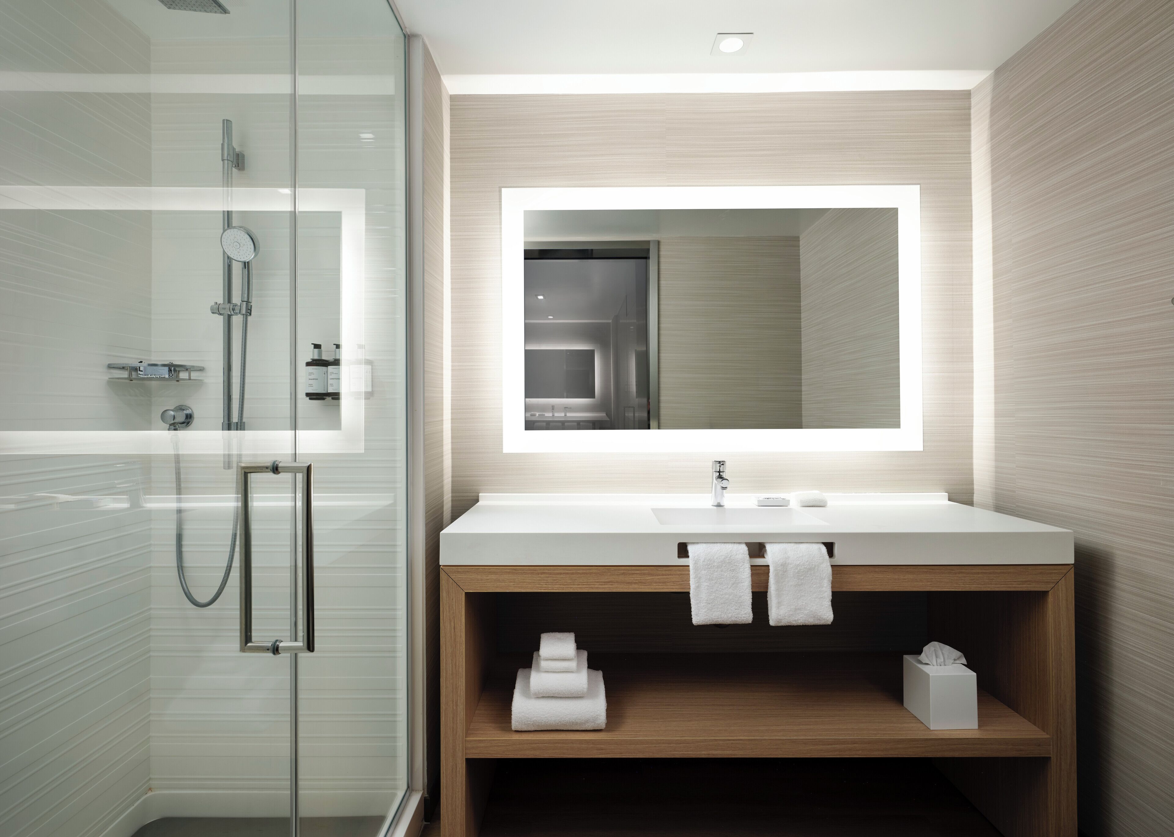 A modern bathroom with a glass shower enclosure, a white sink with a large mirror, and wooden vanity shelves.