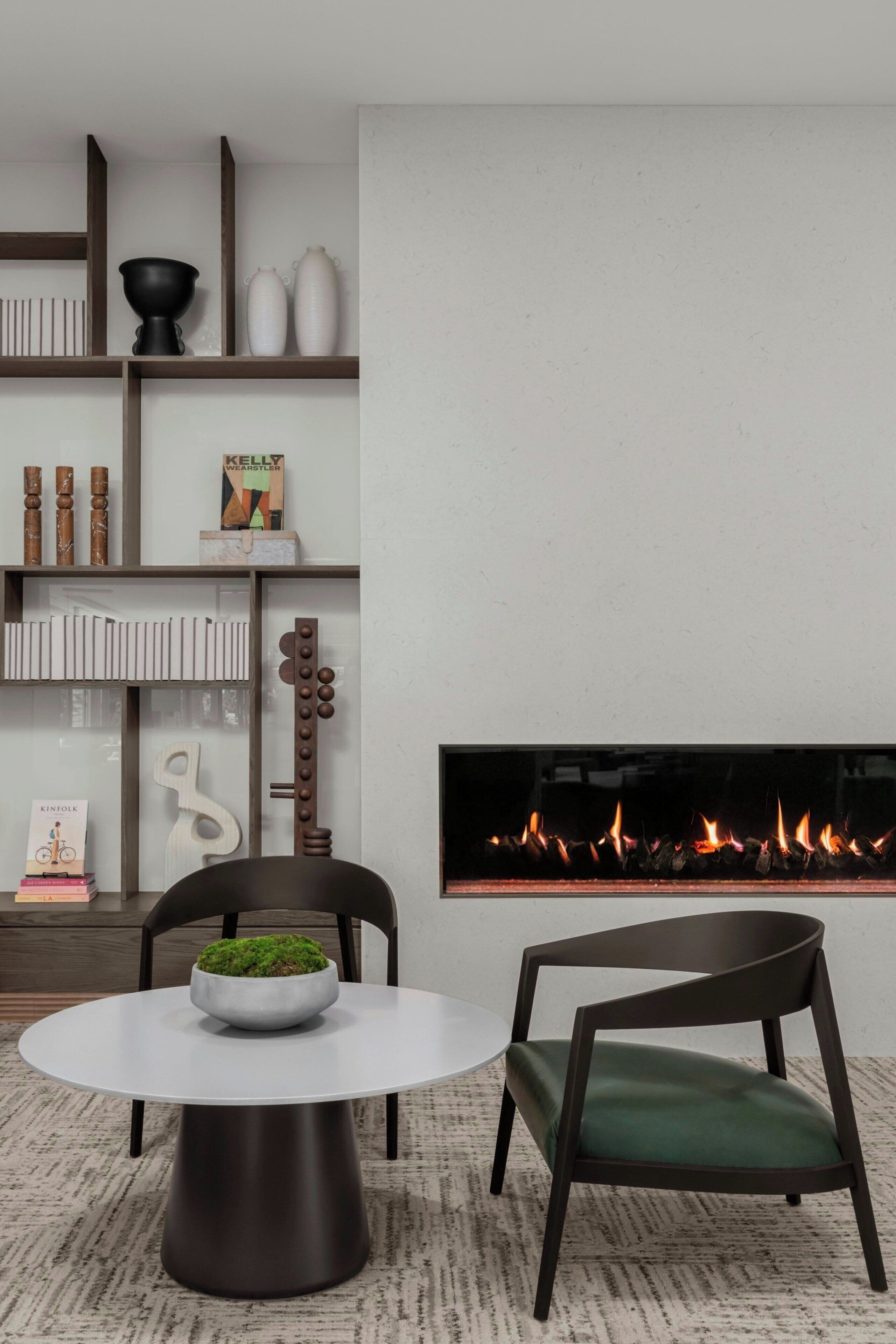 Ein modernes Wohnzimmer mit rundem Tisch, zwei Stühlen, einem Kamin und einem Bücherregal.