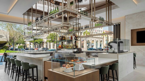 A modern bar area with a central island, bar stools, and a glass display case with pastries. - AC Hotel Pasadena (Pasadena)