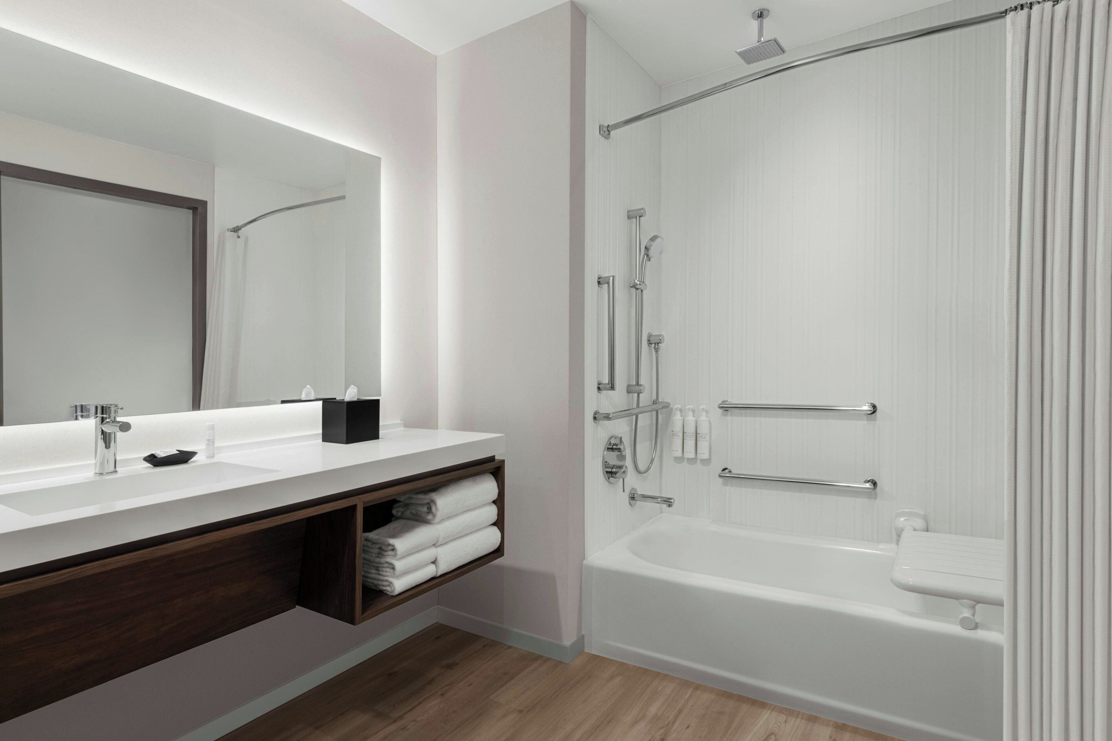 A modern bathroom with a large mirror, a white sink, and a walk-in shower.