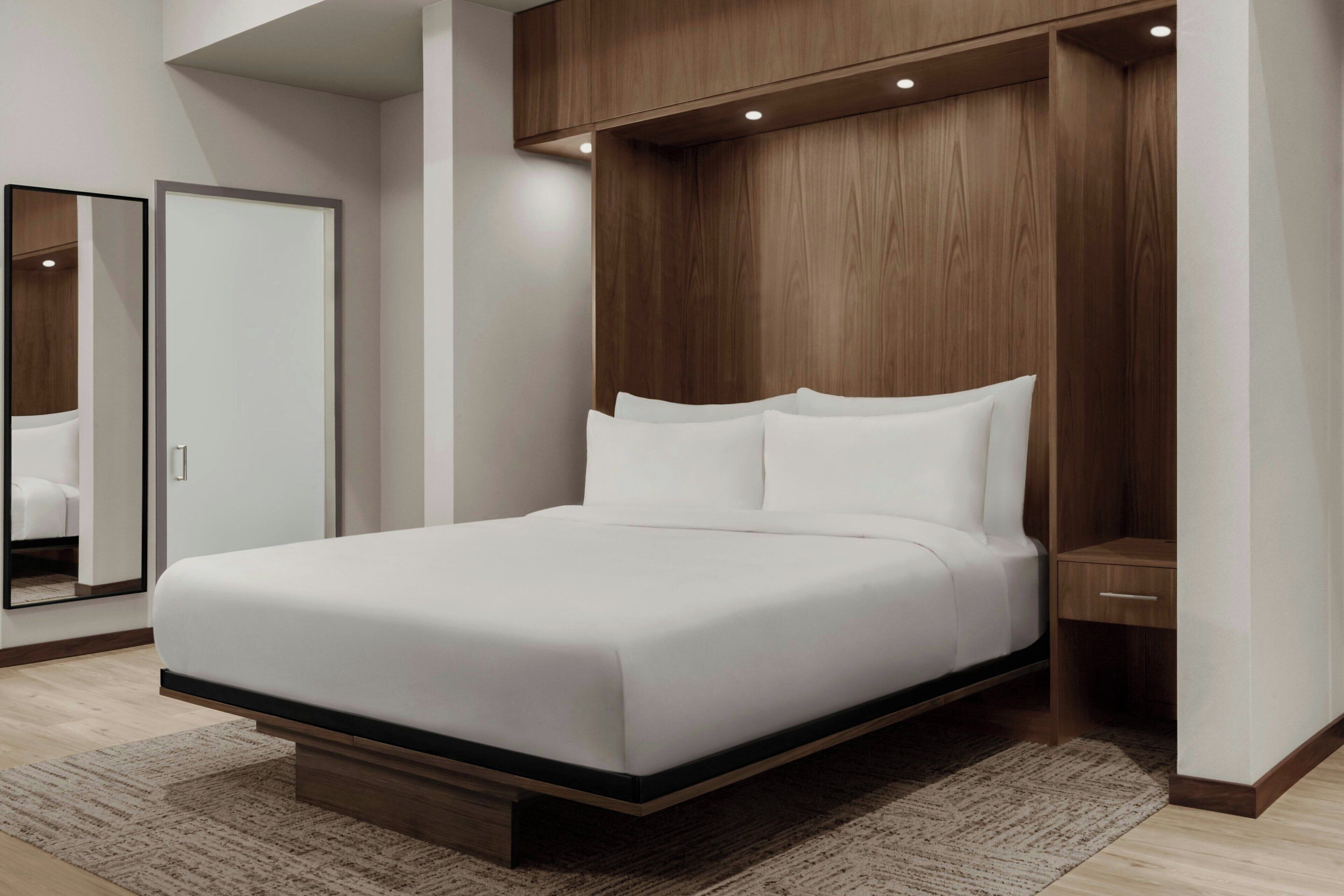 A modern bedroom with a bed, a wooden headboard, a nightstand, and a mirror.