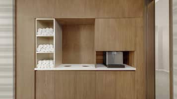 A compact kitchenette with wooden cabinetry, a built-in coffee machine, and neatly rolled towels on shelves.