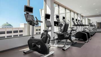 A modern gym with cardio machines, weight stations, and large windows offering city views.