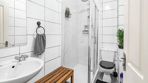 A bathroom with a sink, mirror, towel rack, shower, and toilet. - Urban Haven (London)