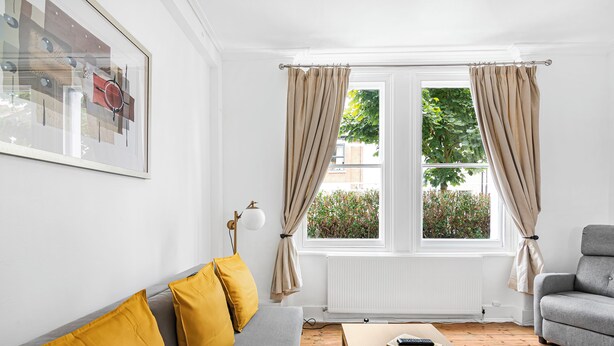 A living room with a grey sofa, yellow cushions, a grey armchair, a wooden coffee table, and a framed picture on the wall. - Urban Haven (London)