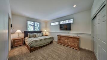 Une chambre à coucher avec un lit, des tables de chevet, une commode, un téléviseur et une fenêtre.