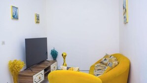A living room with a flat-screen TV, a yellow armchair, and a small wooden coffee table. - HIGH STANDING APARTMENT CI (Abidjan)