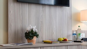Una sala moderna con un televisor de pantalla plana montado en una pared de madera, una pequeña planta en maceta, un frutero y una lámpara.