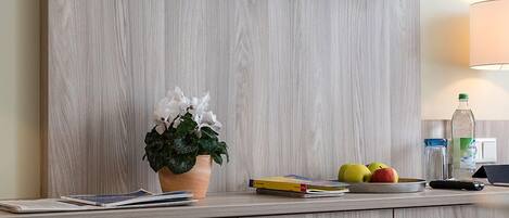 Una sala moderna con un televisor de pantalla plana montado en una pared de madera, una pequeña planta en maceta, un frutero y una lámpara.
