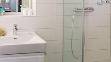 Ein modernes Badezimmer mit Duschkabine aus Glas, einem weißen Waschbecken mit chromfarbener Armatur und einem Spiegel darüber.