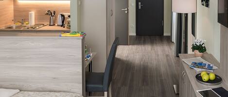 Una habitación de hotel moderna con kitchenette, zona de comedor y un pequeño espacio de trabajo.