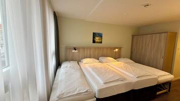 A hotel room with two beds, a wooden wardrobe, and a painting on the wall.