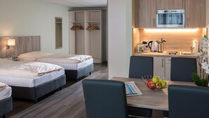 Habitación de hotel con cama, mesita de noche y una pequeña kitchenette equipada con microondas y hervidor.